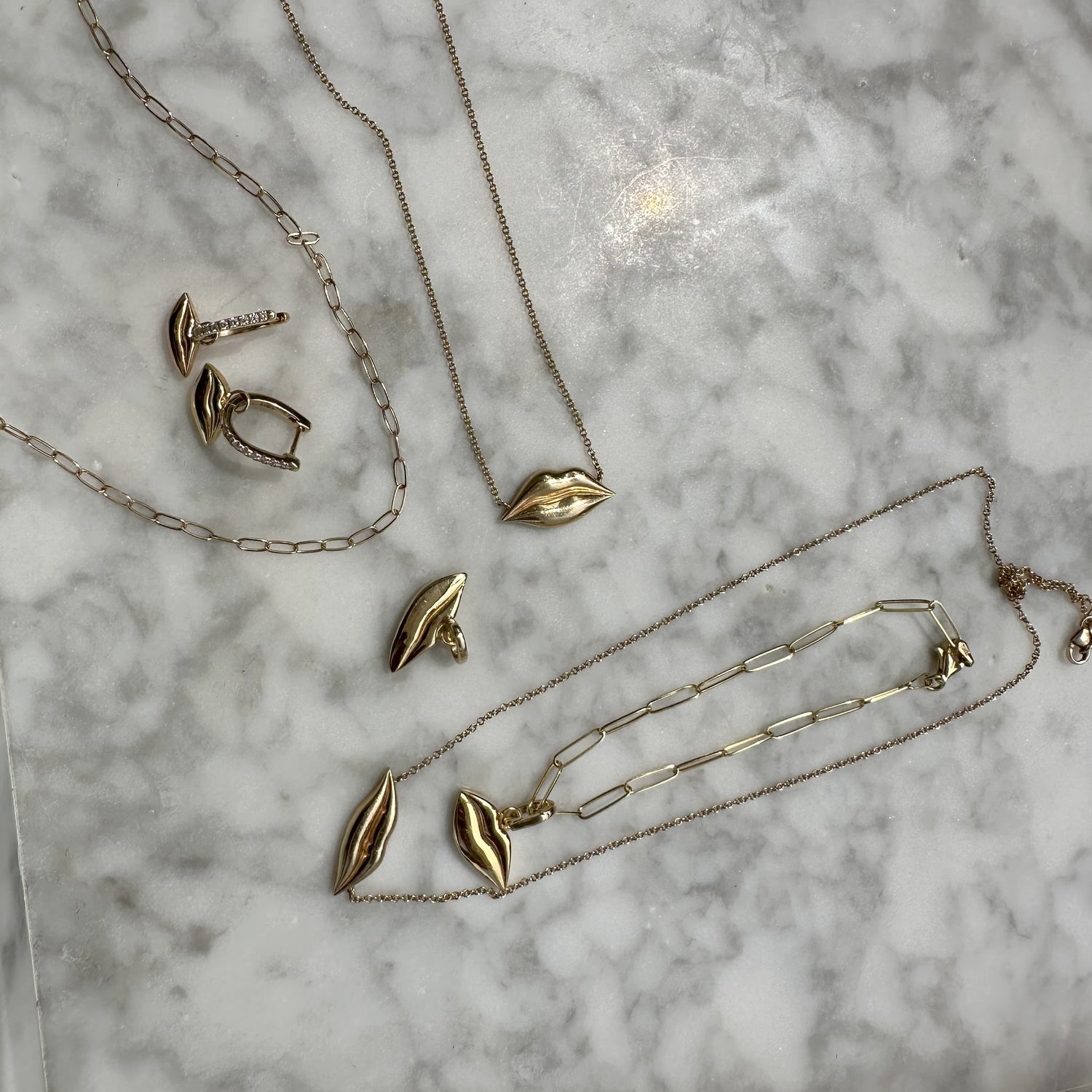 Gold jewelry set including necklaces and earrings on a marble surface